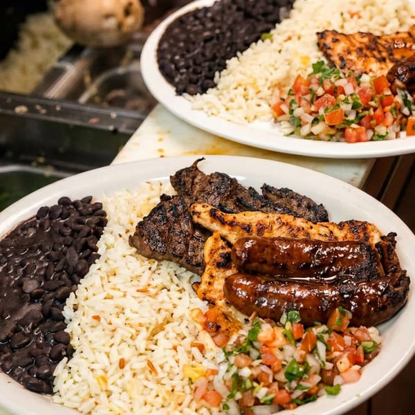 Two grilled meat combo plates with rice, black beans, and pico de gallo on a serving line.