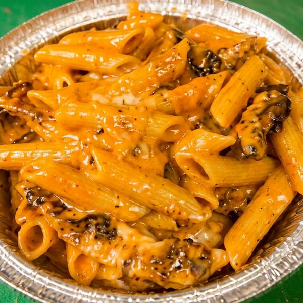 Penne pasta with creamy orange sauce and melted cheese in a foil container on a green surface.