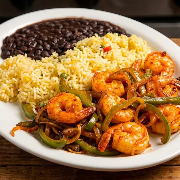 Shrimp fajitas with bell peppers and onions, served with yellow rice and black beans on a white plate.